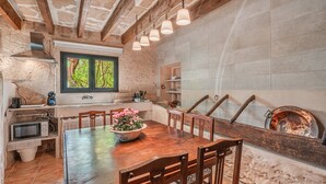 A rustic kitchen with exposed brick walls, a wooden dining table, and a built-in oven. - Apartment "Segles 11" with Shared Pool & Wi-Fi (Campos)