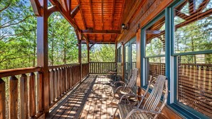 Eine Holzterrasse mit Geländer, Holzstühlen und großen Fenstern.