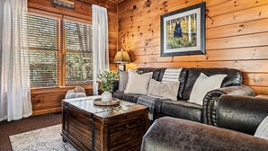 Ein gemütliches Blockhaus-Interieur mit Holzwand, Ledersofa, Holzfach und einem gerahmten Bild an der Wand.