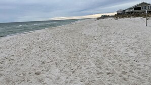 Une plage de sable avec une maison sur pilotis, située à droite.