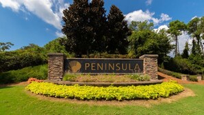Un panneau indiquant « Peninsula », avec un socle en pierre et un emblème solaire, entouré d’un jardin bien entretenu où poussent des fleurs jaunes.