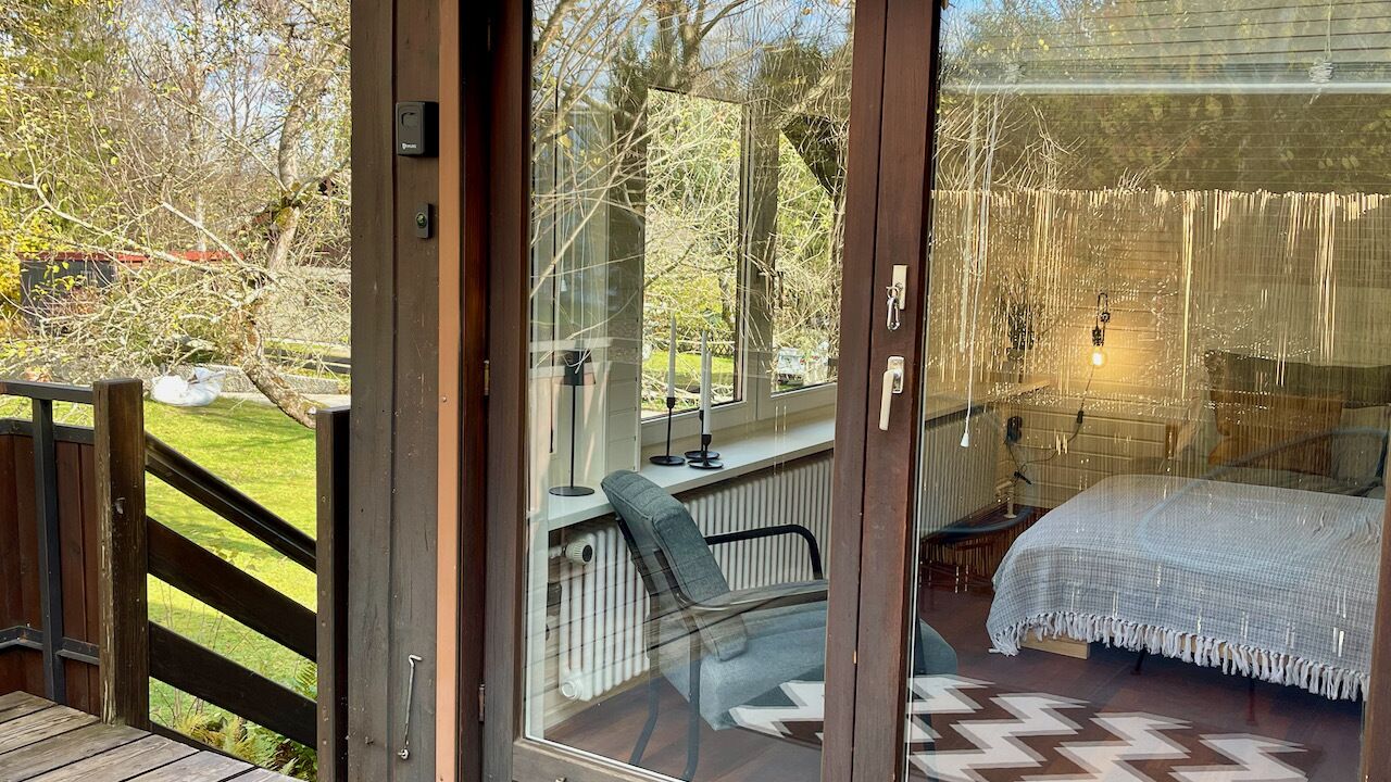 A bedroom with a bed, a chair, and a view of the garden through a glass door.