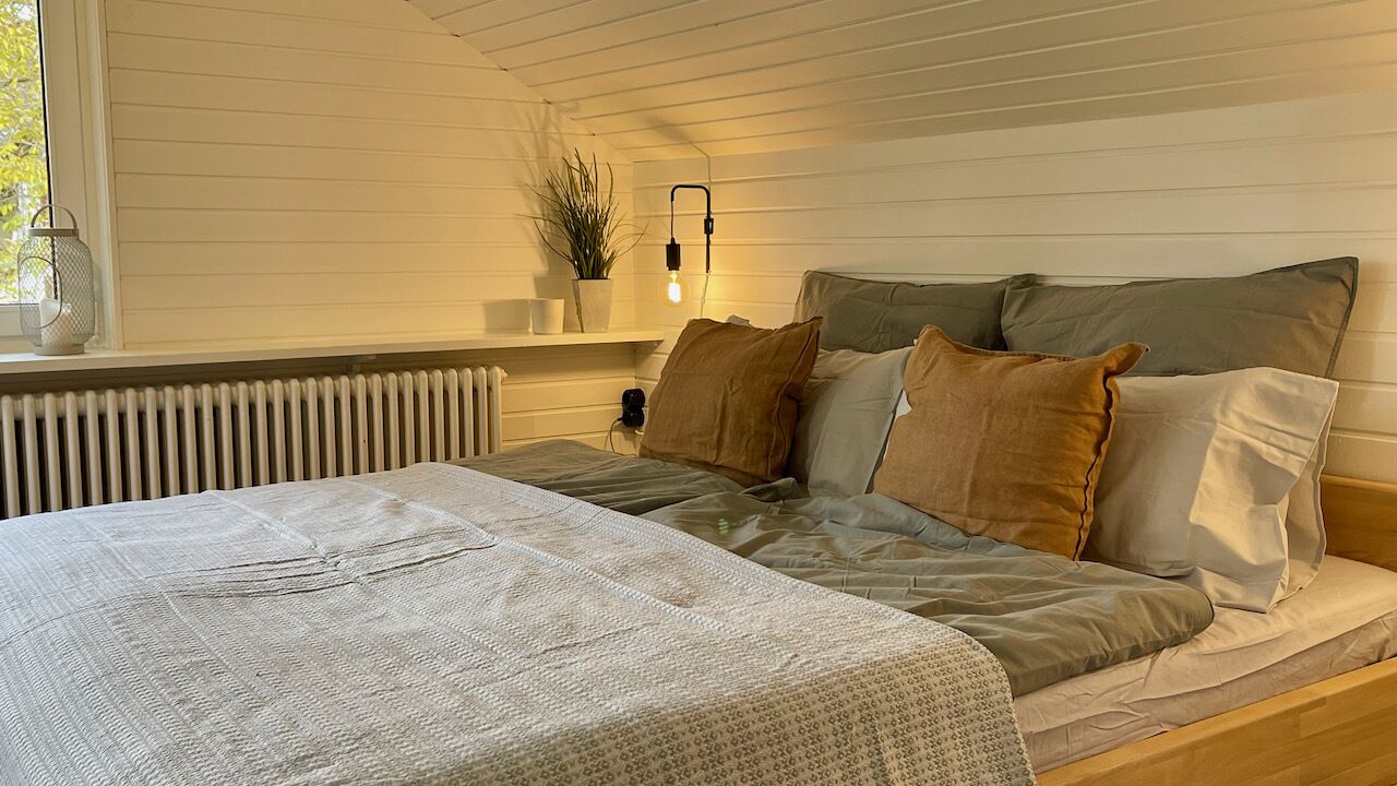 A bedroom with a bed, pillows, a bedside table, a lamp, and a window.