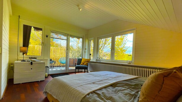 Un dormitorio con cama, cómoda, silla y ventana con vista a árboles.