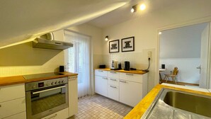 Cocina compacta con horno Bosch, un lavabo y un ventanal con cortinas de encaje.
