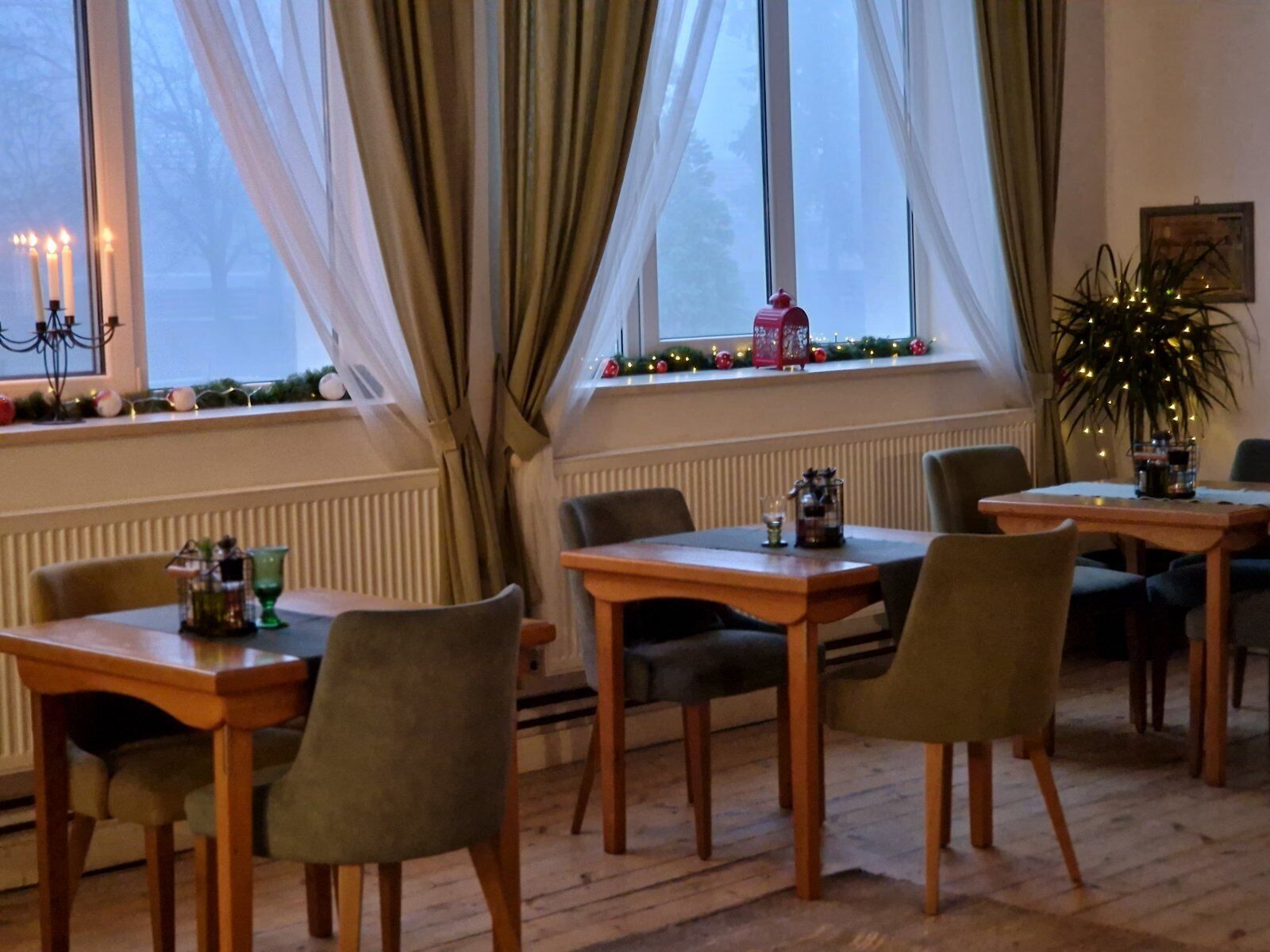 A cozy dining area with wooden tables and chairs, a window with curtains, and a radiator.