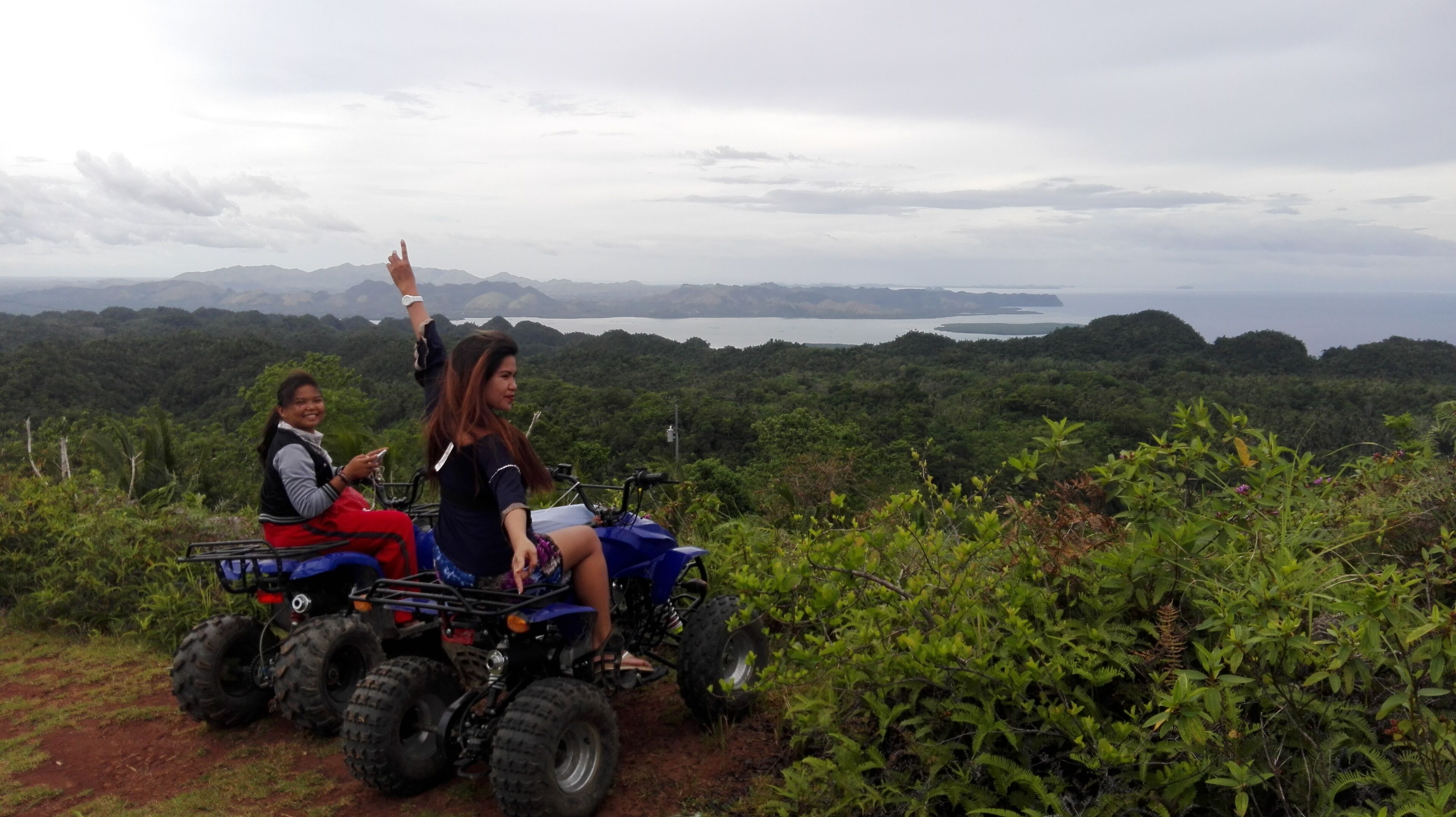 Deux personnes sont assises sur un quad bleu, dans un cadre naturel, avec vue sur un lac et des montagnes.