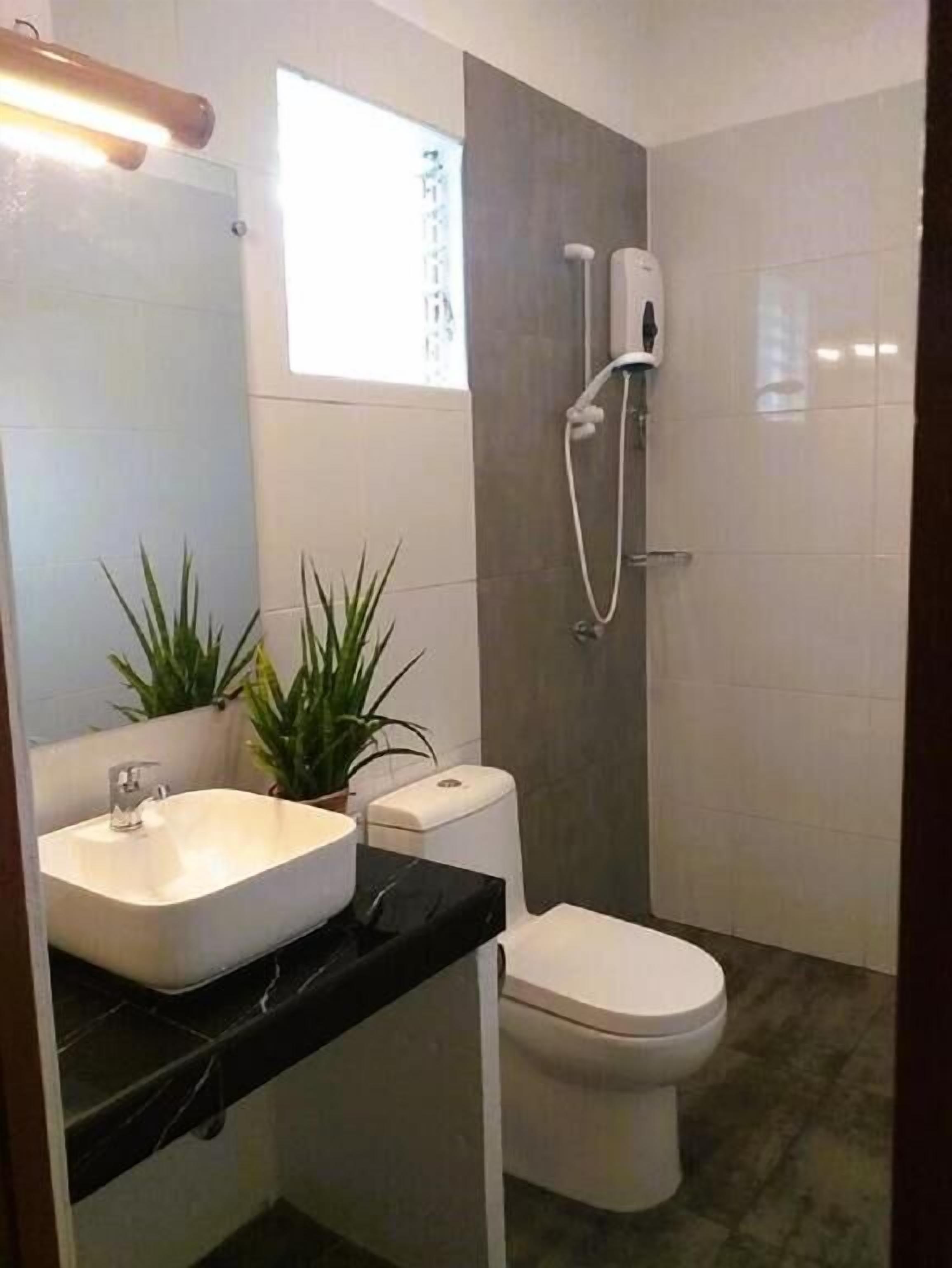 A modern bathroom with a white sink, toilet, and shower. There are two potted plants on the counter.