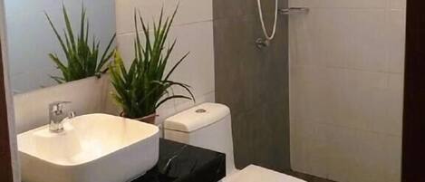 A modern bathroom with a white sink, toilet, and shower. There are two potted plants on the counter.
