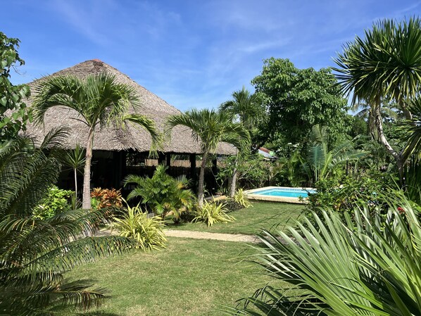 A thatched-roof structure surrounded by lush greenery and a swimming pool. - Cabagnow Seaside Resort (Anda)