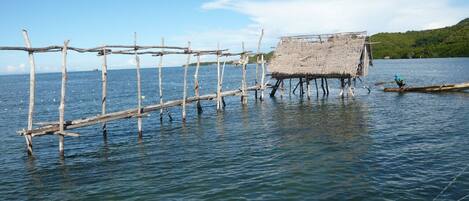 A wooden structure extending into a body of water, with a thatched-roof building at the end.