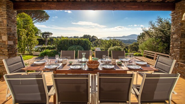 Un'area pranzo all'aperto con un tavolo apparecchiato per sei persone, circondata da mura in pietra e affacciata su un panorama suggestivo.