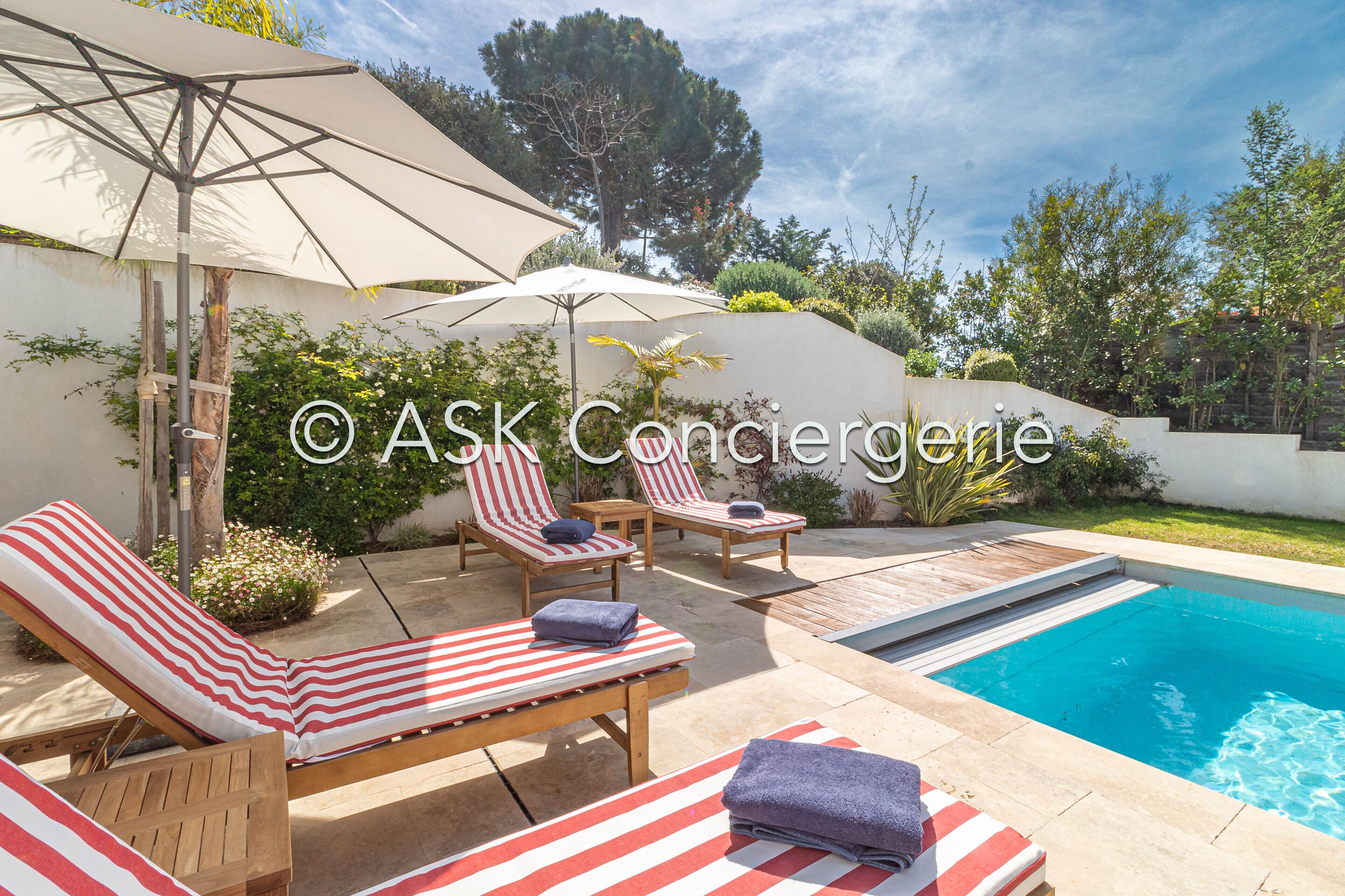 Un espace aménagé au bord de la piscine, avec des chaises longues, des parasols et une piscine.