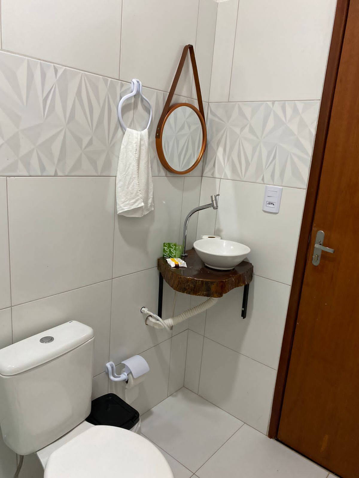A compact bathroom with a toilet, a sink with a wooden shelf, a towel rack, and a mirror.