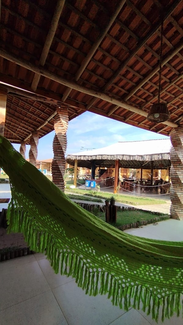 A covered outdoor area with a hammock, brick pillars, and a thatched-roof structure.