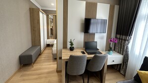 A modern hotel room with a wooden floor, a desk with a laptop, a TV mounted on the wall, and a bed with a bench. - H&L Suites (Istanbul)