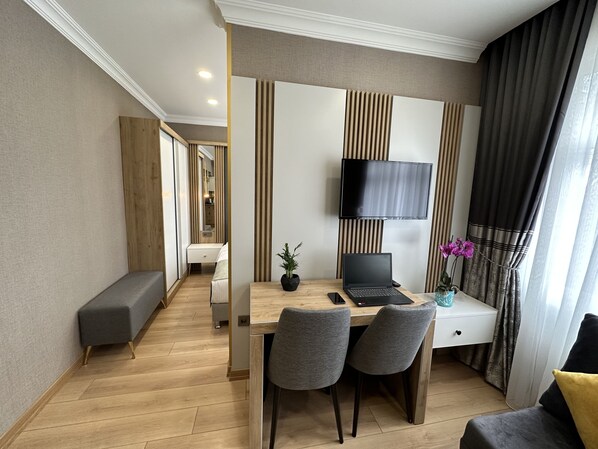 A modern hotel room with a wooden floor, a desk with a laptop, a TV mounted on the wall, and a bed with a bench. - H&L Suites (Istanbul)