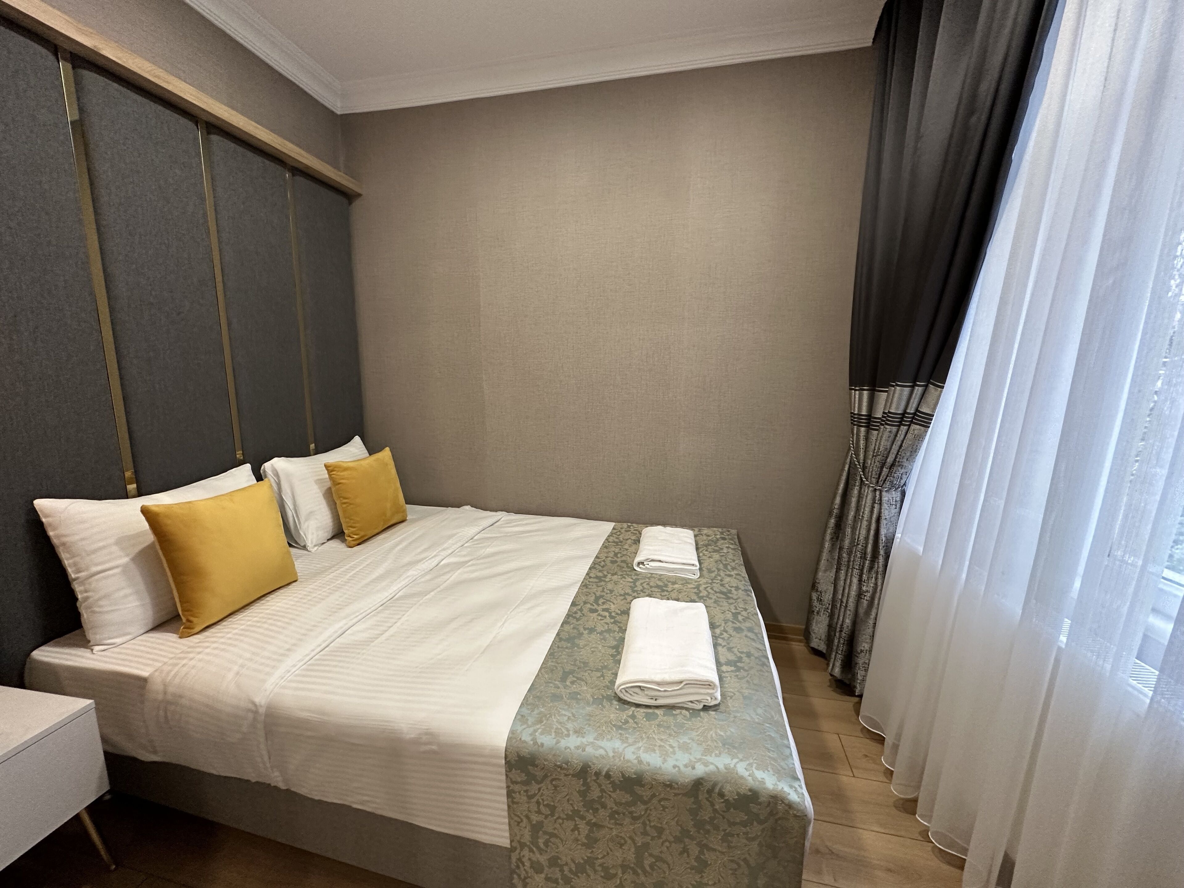 A hotel room with a large bed, a bedside table, and a window with curtains.