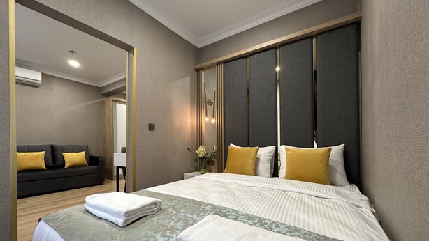 A modern hotel room with a large bed, a sofa, and a mirror. - H&L Suites (Istanbul)