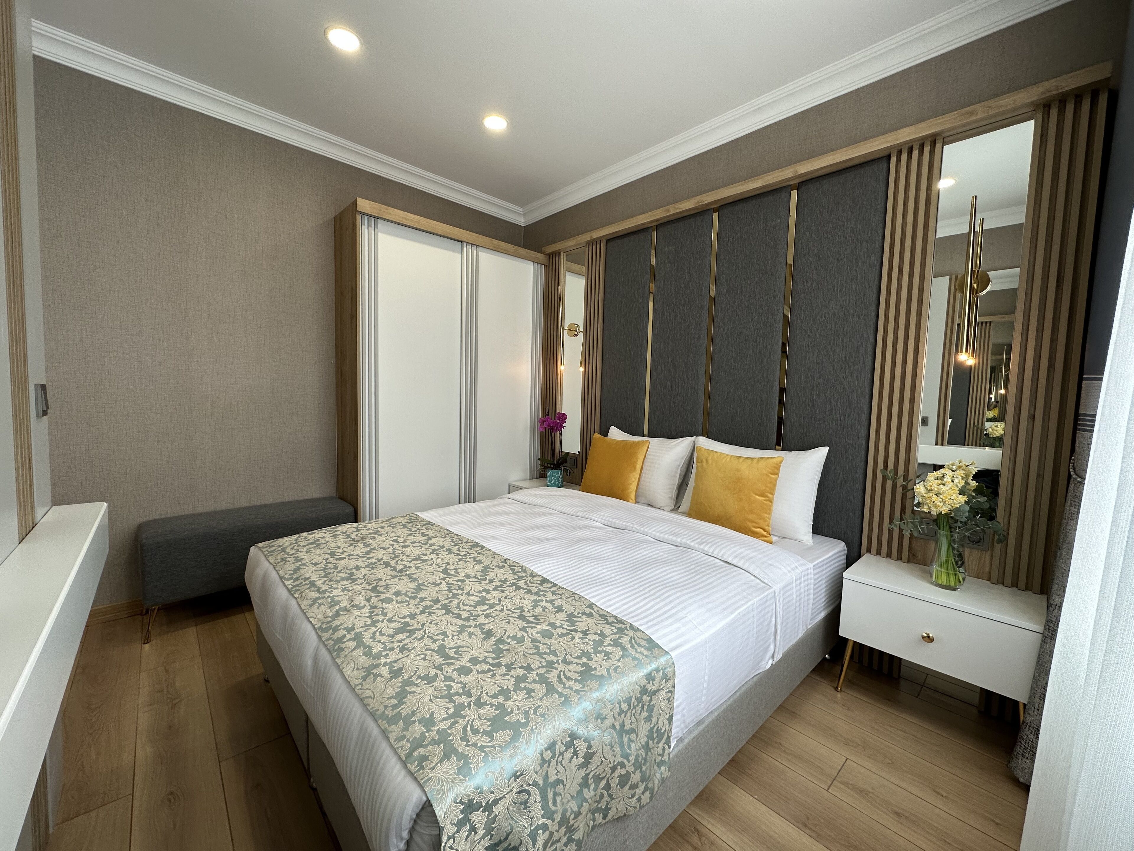 A modern hotel room with a large bed, a bedside table, a mirror, and a wardrobe.