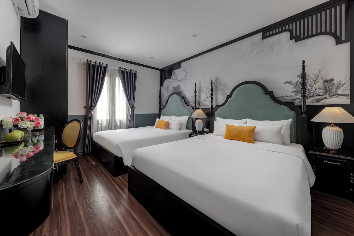 Quarto de hotel com duas camas, uma escrivaninha, uma cadeira, uma televisão e um mural na parede.