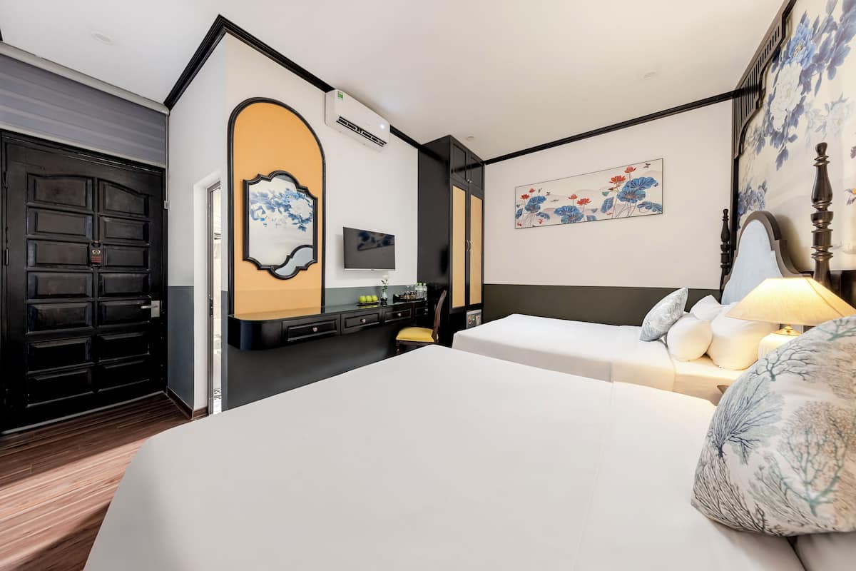Quarto de hotel com uma cama grande, uma escrivaninha com cadeira, televisão e obras de arte nas paredes.