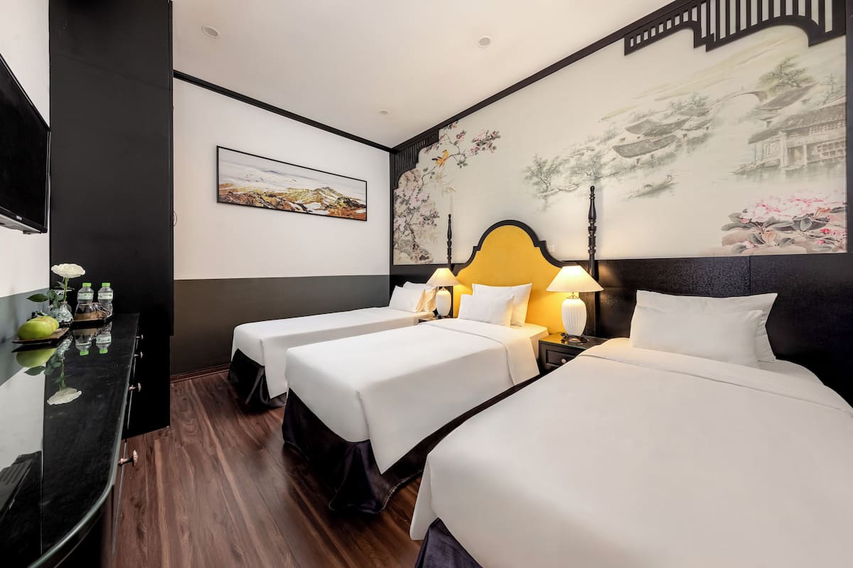 Quarto de hotel com duas camas, televisão, quadro e piso de madeira.