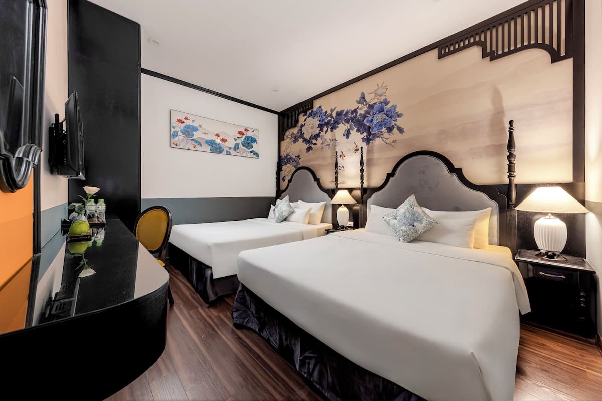 Quarto de hotel com duas camas, uma escrivaninha com espelho, televisão e obras de arte nas paredes.