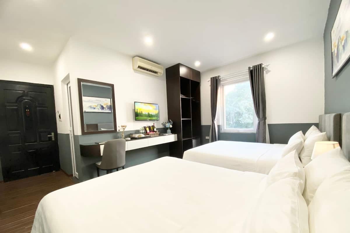 Quarto de hotel com duas camas, uma escrivaninha com computador, televisão e janela com cortinas.