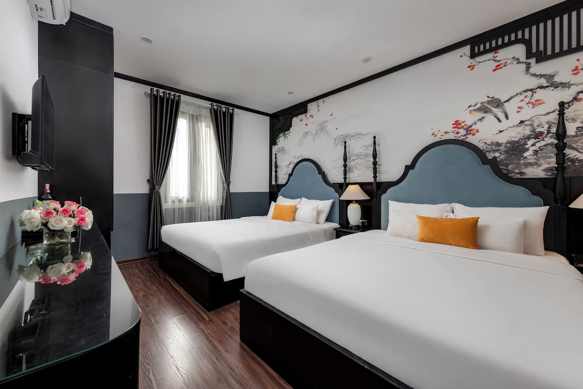 Quarto de hotel com duas camas, televisão, escrivaninha com um vaso de flores e um mural na parede.