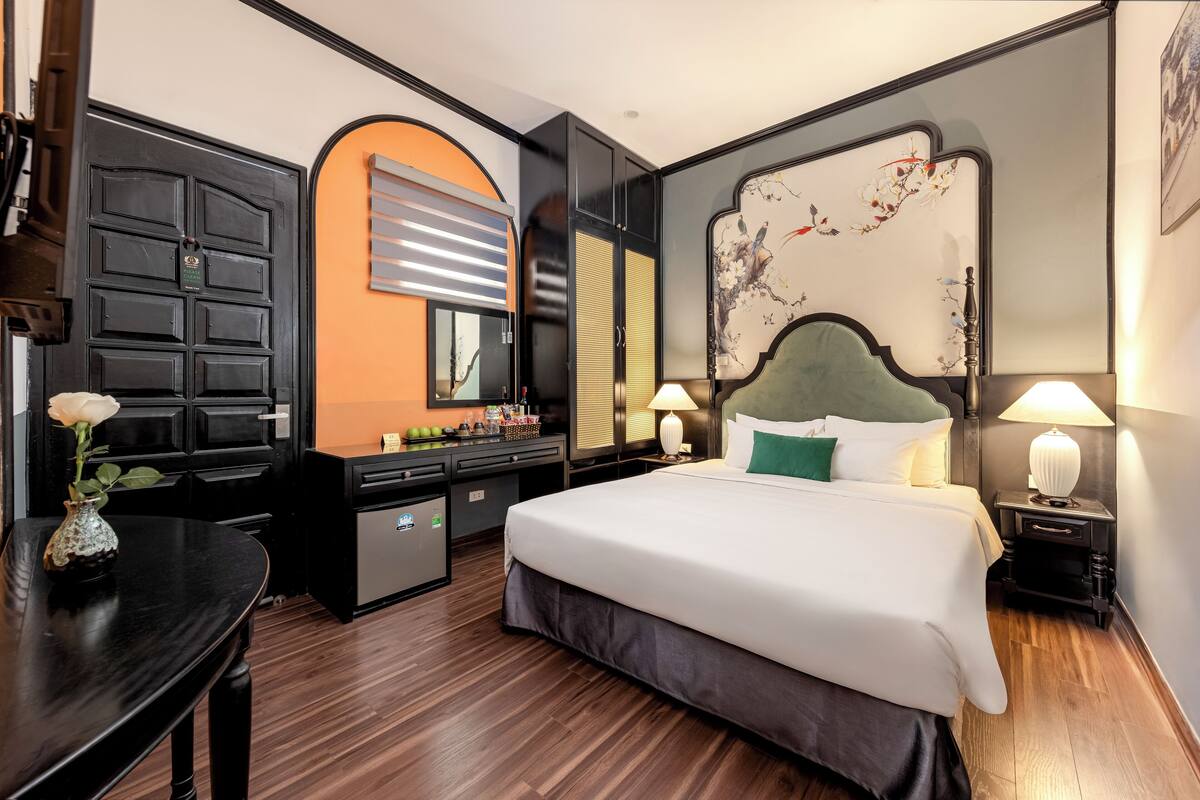 Quarto de hotel com uma cama grande, uma escrivaninha, um penteou e um espelho.