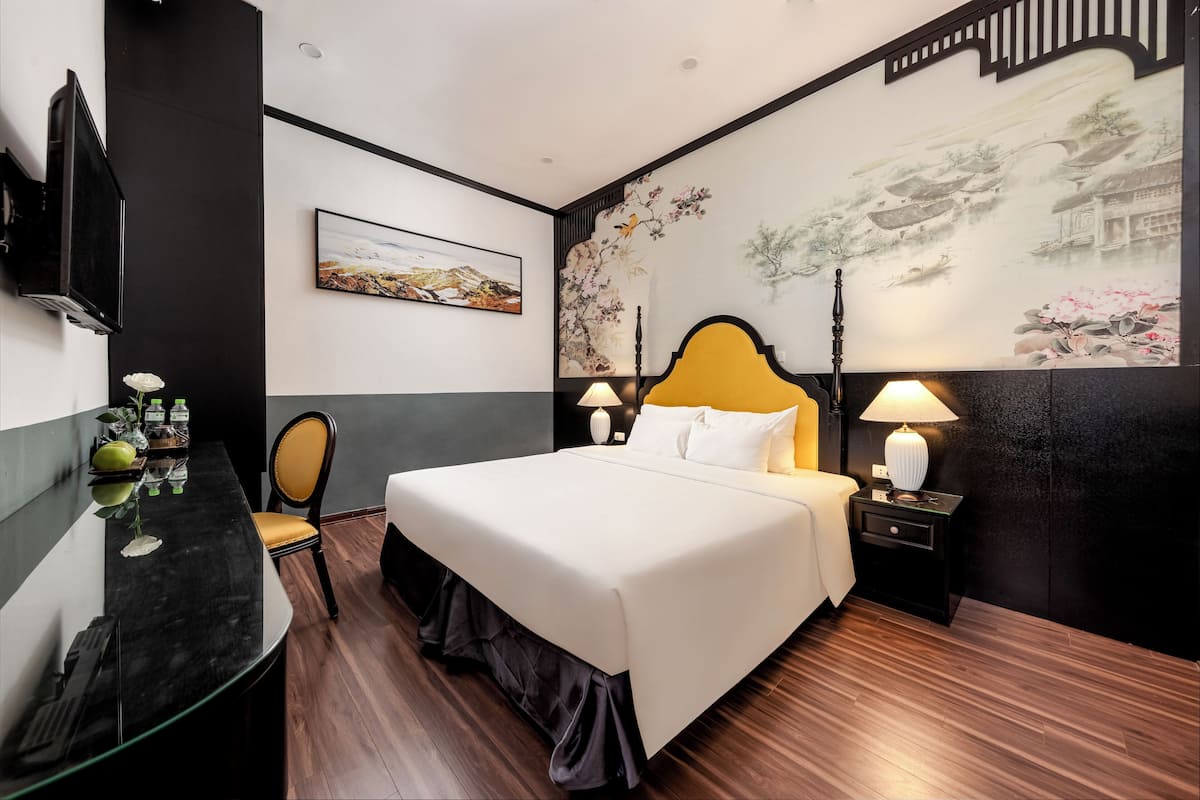 Quarto de hotel com uma cama grande, uma escrivaninha com cadeira, televisão na parede e obras de arte nas paredes.