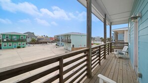 A wooden deck with a railing, overlooking a parking lot and several buildings. - Just Wanna Have Sun, Game Room, Pool & Beach (Port Aransas)