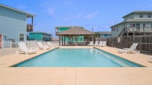 A swimming pool with lounge chairs, a covered seating area, and adjacent buildings. - Just Wanna Have Sun, Game Room, Pool & Beach (Port Aransas)