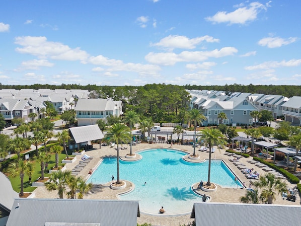 A resort with a central swimming pool surrounded by palm trees and lounge chairs.