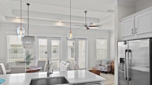 Une cuisine moderne dotée d’un réfrigérateur en acier inoxydable, d’un îlot central avec un évier, de luminaires suspendus et d’un ventilateur de plafond.