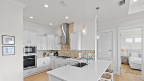 Une cuisine moderne avec des meubles blancs, un îlot central et des luminaires suspendus.