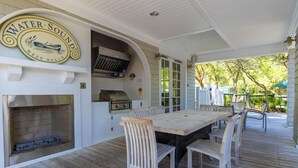 Une terrasse extérieure avec une table et des chaises en bois, un barbecue et un panneau indiquant « Water Sound West Beach ».