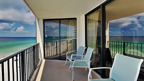 Un balcón con vista al océano y la playa, con dos sillas y una mesa.