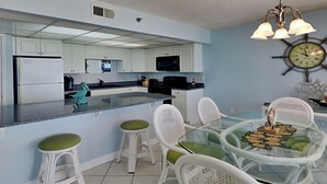 Una cocina moderna con armarios blancos, un microondas negro y una isla de cristal con taburetes de bar.