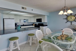 Una cocina moderna con gabinetes blancos, un microondas negro y una isla de vidrio con taburetes.