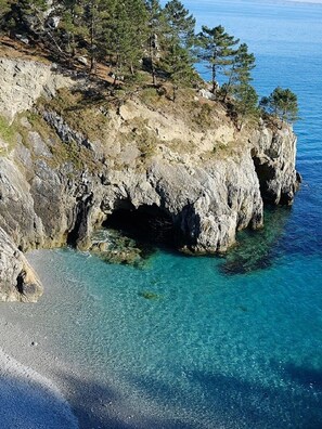 Una costa rocosa con aguas turquesas cristalinas, una playa estrecha y vegetación escasa.