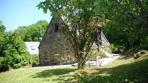 Un edificio de piedra con techo inclinado, rodeado de follaje y árboles.