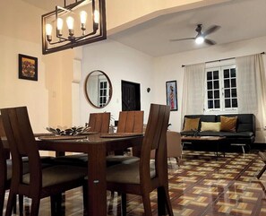 Comedor con una mesa y sillas de madera, ventilador de techo y suelo estampado.