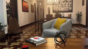 Ein Wohnzimmer mit einer Couch, einem Couchtisch und einem gemusterten Boden. An der Wand hängt ein Gemälde, und eine Chandeliebre ziert die Decke.
