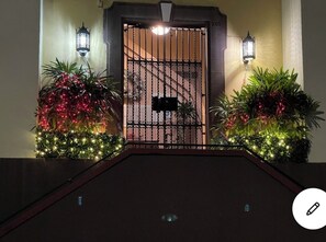 A gated entrance with a metal gate, two wall-mounted lanterns, and potted plants with lights. - Cozy, Classic & Gorgeous Apt near Condado beach 5 bedrooms 3 bathrooms 1Parking (San Juan)
