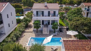 Una casa de dos pisos con piscina, rodeada de vegetación y un barco al fondo.