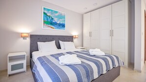 Un dormitorio ordenado con una cama grande, un armario blanco y un cuadro de una escena costera.