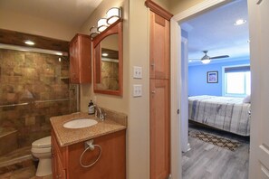 A bathroom with a granite countertop sink, a glass shower enclosure, and wooden cabinets.