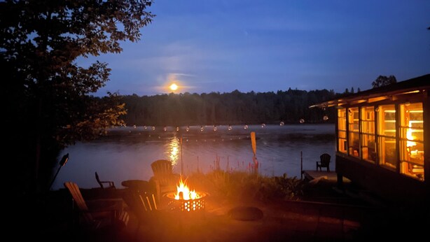 A lakeside cabin with a fire pit, outdoor seating, and a view of the lake and forest.
